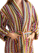 Load image into Gallery viewer, A close-up of a person wearing a chunky knit robe with vertical stripes of multicolored yarn-like texture in pink, yellow, green, orange, blue, and purple on a white background.
