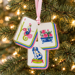 Load image into Gallery viewer, A decorative hanging ornament shaped like stacked playing cards, suspended from a pink ribbon on a Christmas tree with warm lights in the background. The cards feature colorful illustrations, including a green and pink snail, pink flowers in a blue pot, and a blue-and-white dog.

